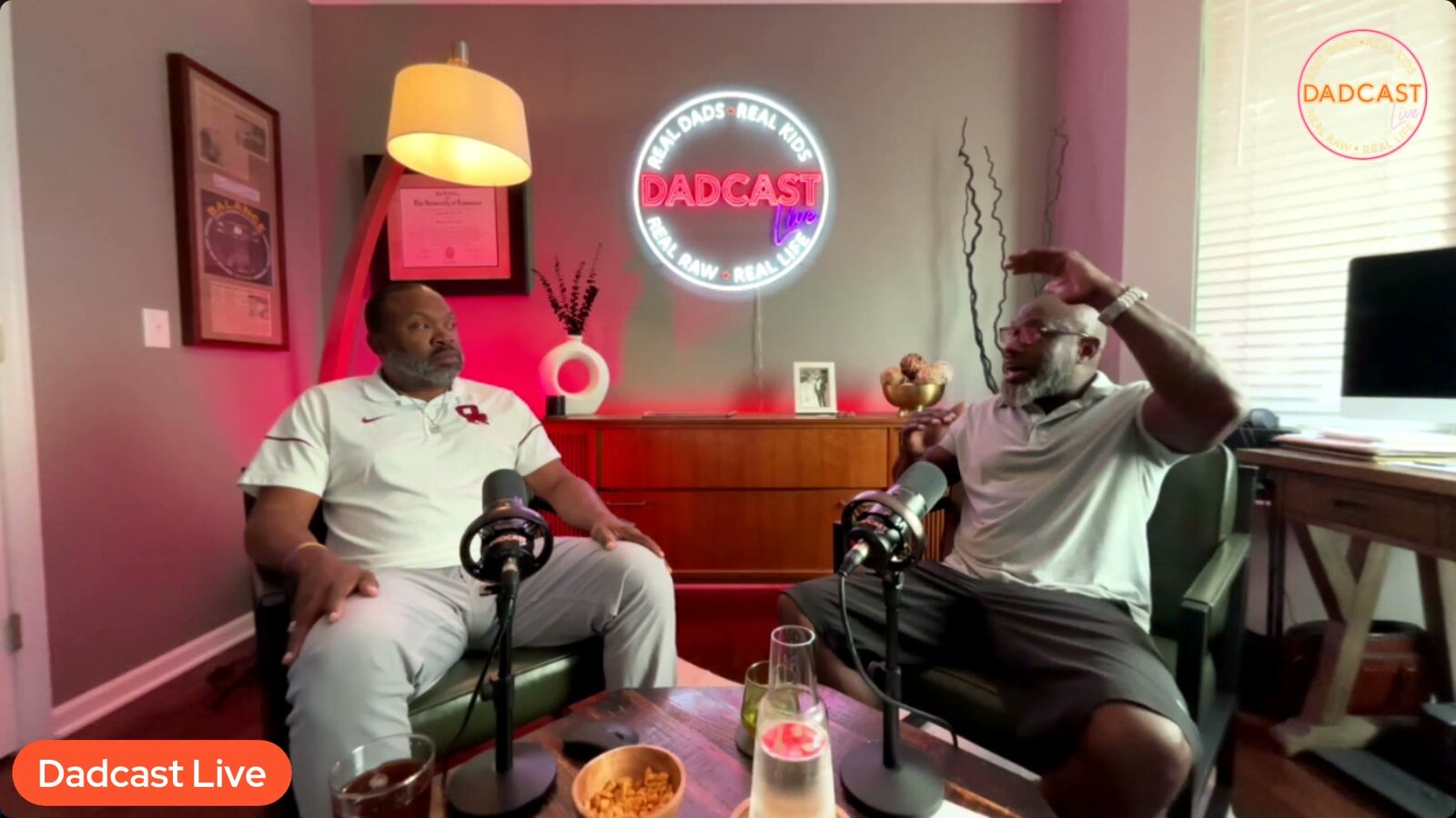 Oz Episode 1: two men in the Dadcast Live studio, warm-lit with the neon sign glowing between them