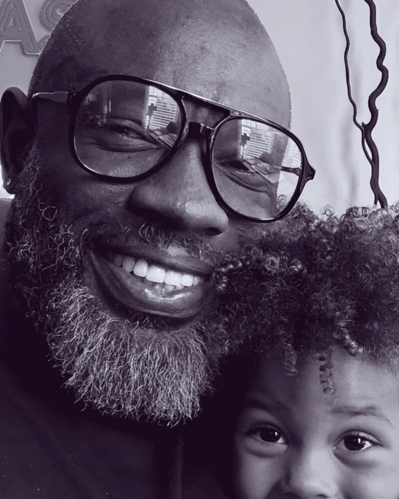 Russ, host of Dadcast Live, in the studio with his kid, smiling in front of the DADCAST neon sign
